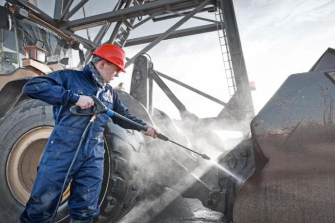 Worker performing high-pressure cleaning on heavy mining equipment to remove dirt and residue