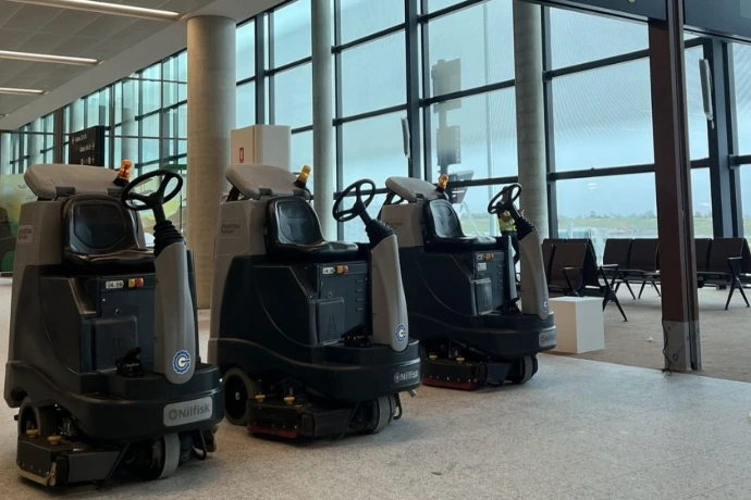 Ride-on scrubbers for hangar and terminal maintenance Ride-on scrubbers positioned inside an airport hangar or terminal for large-scale aviation floor maintenance