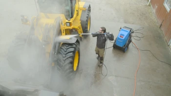 Worker cleaning around heavy machinery using site-maintenance equipment to manage dust and debris in mining areas