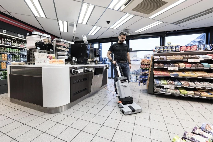 Operator using a floor scrubber to clean supermarket aisles between shelves